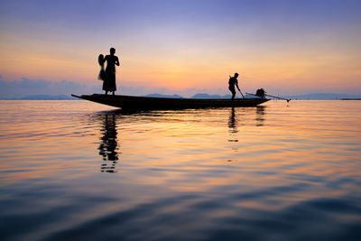 Silhouette people on boat in sea against sky during sunset