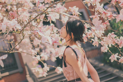 Rear view of woman standing by pink flowering tree