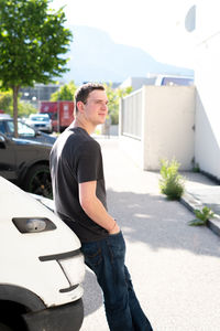 Side view of young man standing by car