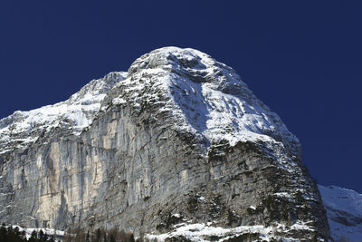 Low angle view of snowcapped mountain against clear blue sky