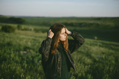 Woman looking away while standing on green landscape against sky during sunset