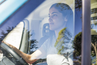 Confident young female owner driving food truck seen through window