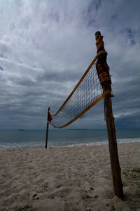 Volleyball net on sandy beach against cloudy sky