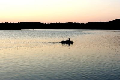 Silhouette boat sailing on lake against sky during sunset