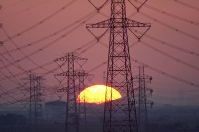 Low angle view of electricity pylon against sky during sunset