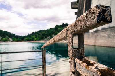 Rusty railing by river against sky