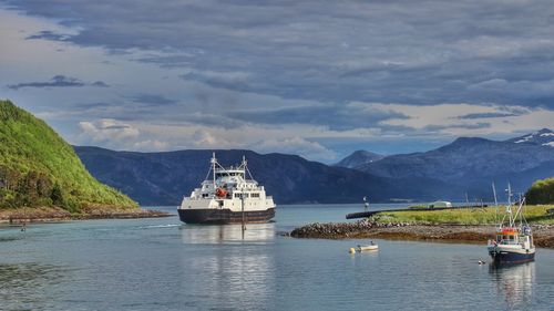 Boat and ship sailing in river by mountains against sky