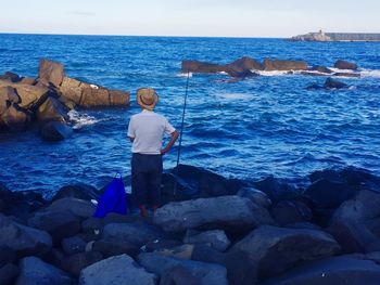 Rear view of man fishing at sea shore