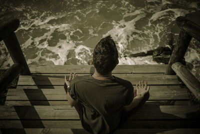 Rear view of man doing yoga on steps against sea