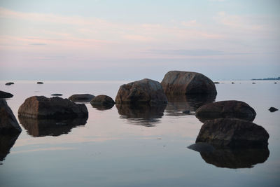 Rocks in sea against sky during sunset