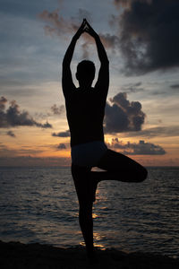 Silhouette yoga man standing at beach against sky during sunset