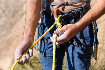 Midsection of shirtless man wearing safety harness while standing outdoors