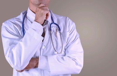Midsection of doctor with stethoscope standing against gray background