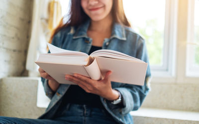 Midsection of woman reading book while sitting at home