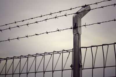 Low angle view of barbed wire fence against sky