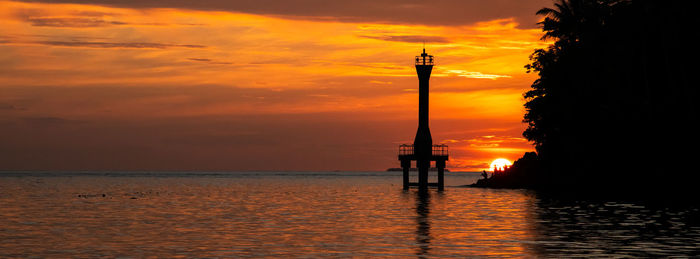 Silhouette lighthouse by sea against sky during sunset