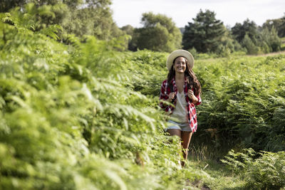 Smiling woman walking amidst green plants at cannock chase on sunny day