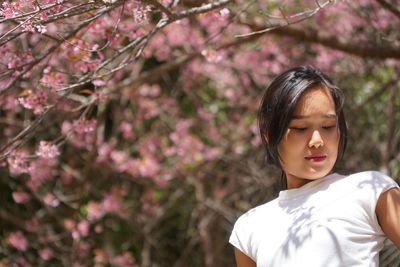 Low angle view of young woman against cherry trees