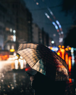 Rear view of woman with umbrella on street at night