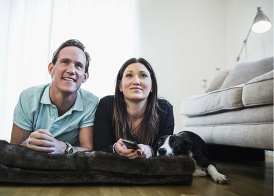 Couple with dog watching tv while lying on floor at home