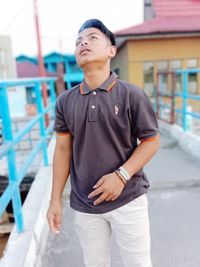 Young man looking away while standing against building