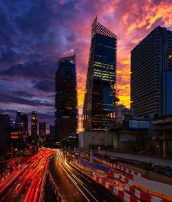 Light trails on illuminated buildings in city against sky during sunset