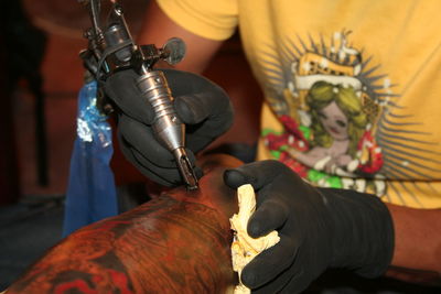 Midsection of tattoo artist tattooing on customer hand