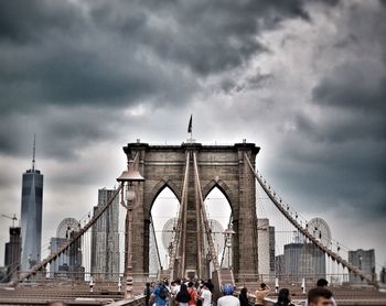 Tourists on brooklyn bridge against cloudy sky