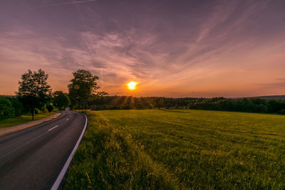 Road amidst field against sky during sunset