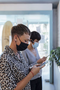 Young woman wearing protective face mask using mobile phone while standing in restaurant during covid-19