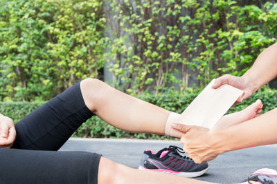 Cropped hands of person wrapping bandage on woman leg against plants