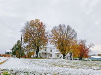 Trees and houses on field against sky during winter