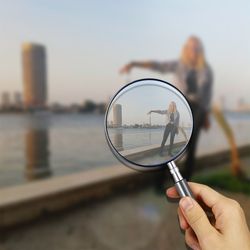 Digital composite image of hand holding magnifying while girl seen through it