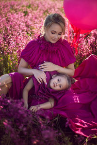 Happy family mom and daughter kiss in pink dresses are sit in a field with flowers and big balloons