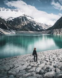 Man standing on rock by lake against sky