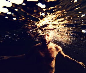 Shirtless man with eyes closed swimming in sea