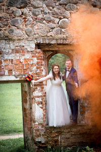 Full length of newlywed couple standing by abandoned built structure