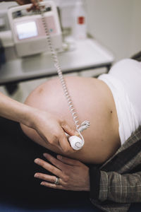 Hands of female gynecologist doing ultrasound of patient's pregnant belly in medical clinic