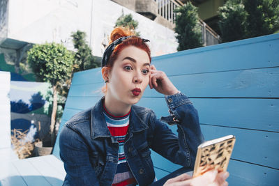 Redhead young woman taking selfie with mobile phone while sitting on bench