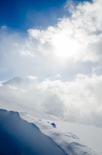 Scenic view of snowcapped mountains with bright light through clouds against sky