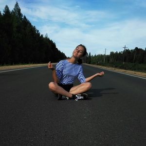 Teenage girl meditating on road against sky