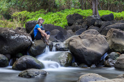 Full length of woman relaxing on rocks by stream at forest