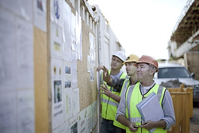 Three male construction workers inspecting bulletin board at construction site