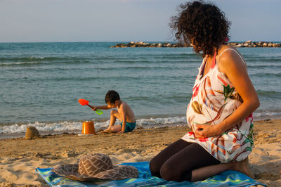 Pregnant mother looking son playing on shore at beach