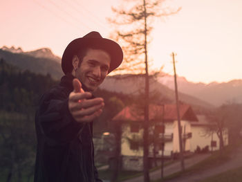 Portrait of smiling young man gesturing while standing against houses and mountains