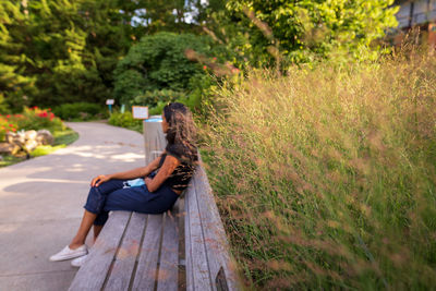 Side view of woman sitting on park bench in public park