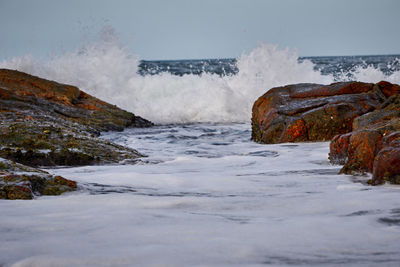 Scenic view of sea waves splashing on rocks against sky