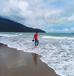 A red-shirt teenager walking towards the wave of the sea in telok melano. captured in 2019.