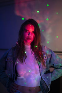 Portrait of young woman standing against illuminated wall