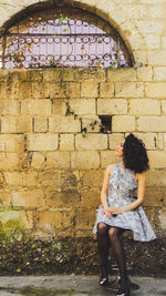 Young woman sitting against wall
